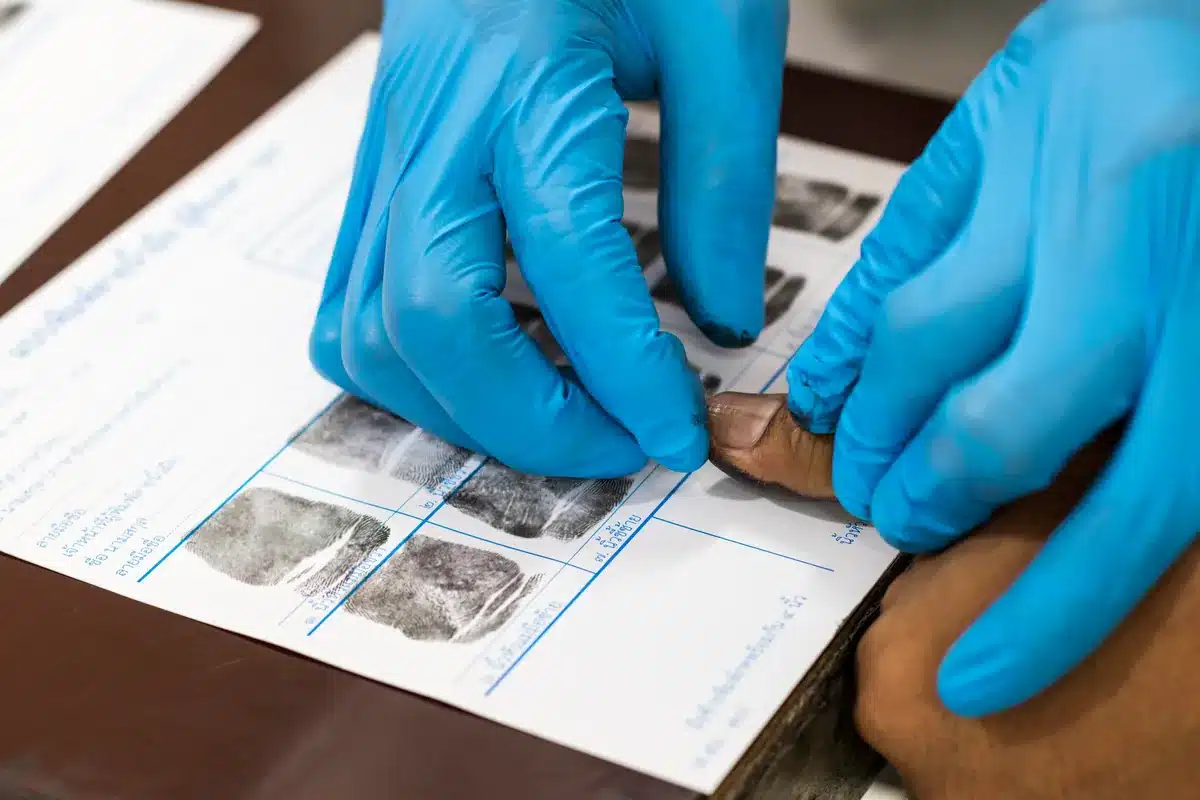 Technician assisting client with ink fingerprinting on FD-258 card for FBI background check.