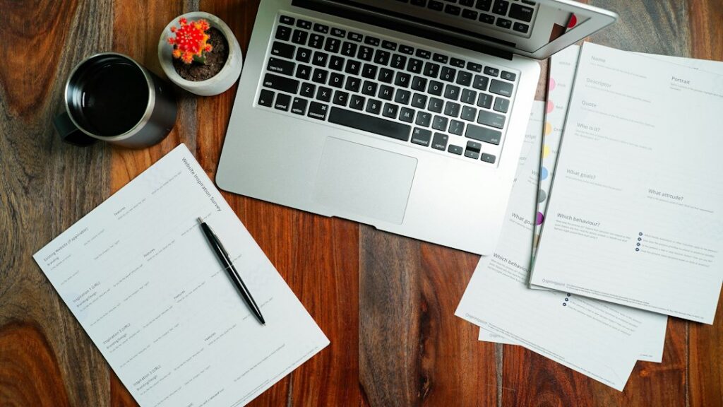 Laptop and documents on a wooden desk, representing out-of-state licence fingerprint cards